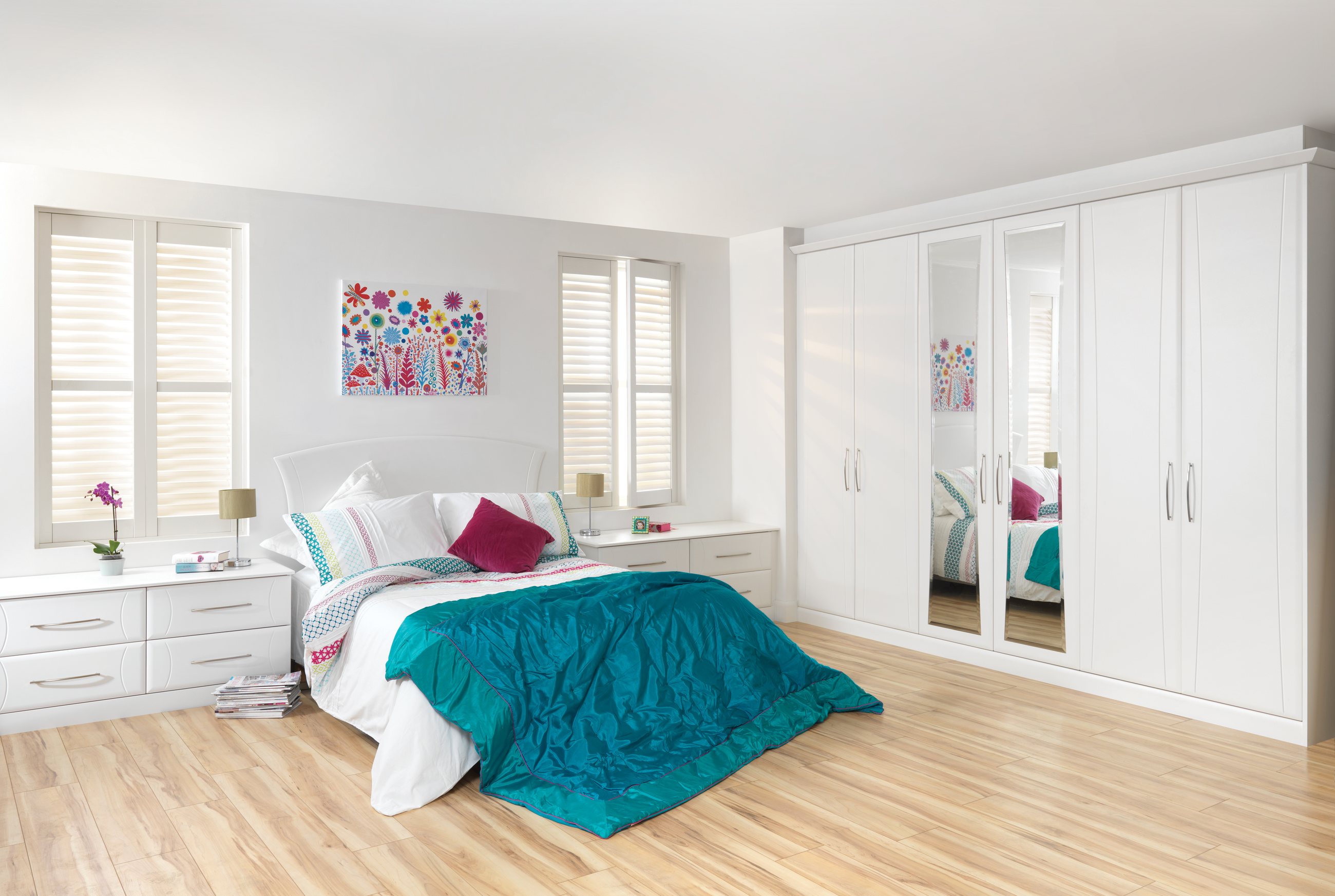 A white fitted wardrobe run in a bright bedroom with mirrored doors